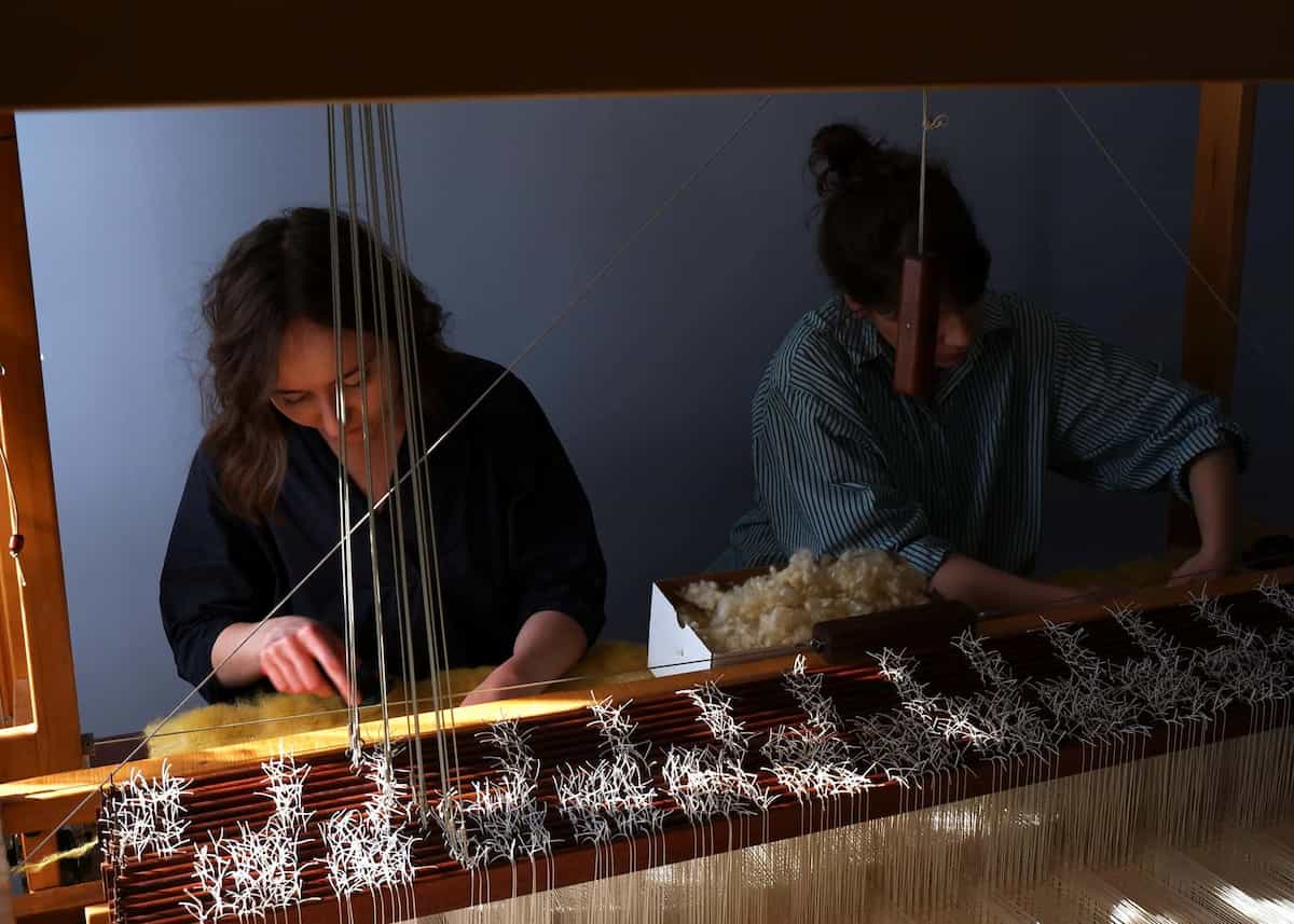 Dominika and Julia are weaving fabric on a loom